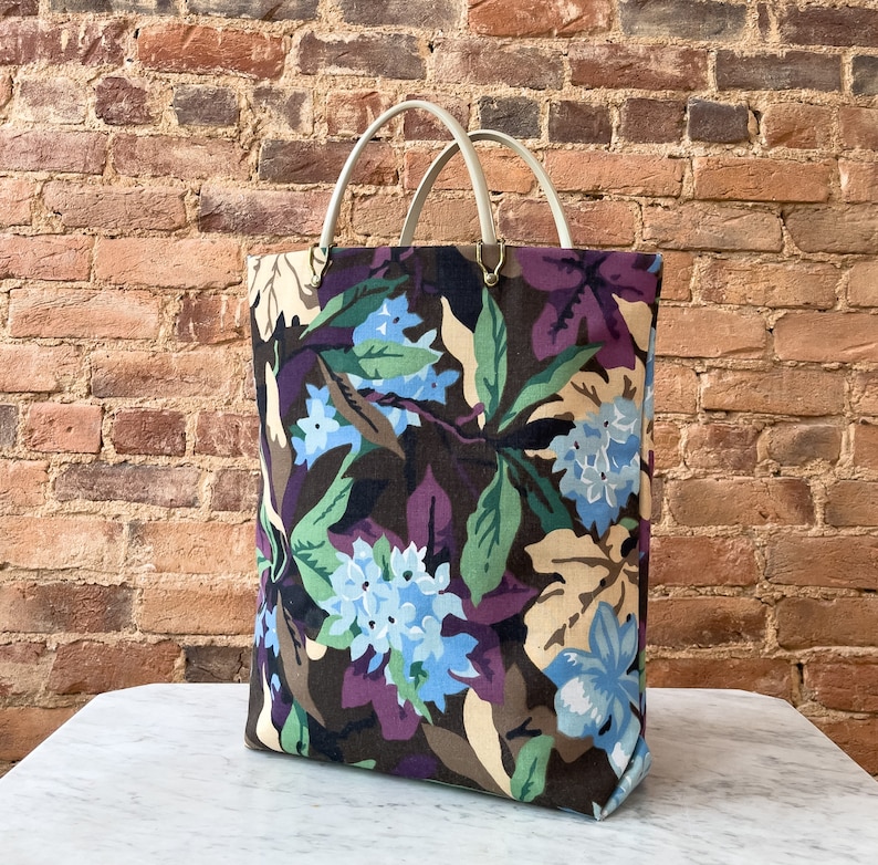 May include: A large tote bag with a floral print featuring blue, green, and brown colors. The bag has two white leather handles.