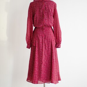 May include: A long-sleeved, red dress with a white floral pattern. The dress has a ruffled collar and a button-up closure in the back.
