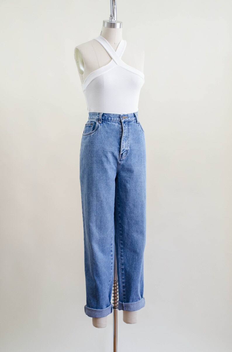 May include: A white halter top and light blue denim jeans displayed on a mannequin. The jeans have a high waist and are cuffed at the ankles. The top has a criss-cross design.