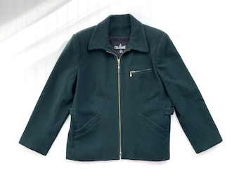 Puede incluir: Una chaqueta verde oscuro con cremallera, cuello y dos bolsillos. La chaqueta tiene una cremallera dorada y una etiqueta que dice "Colebrook" en el lado izquierdo del cuello.