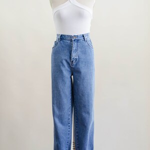 May include: A white halter top and blue denim jeans displayed on a mannequin. The top has a criss-cross design. The jeans are cuffed at the ankles.