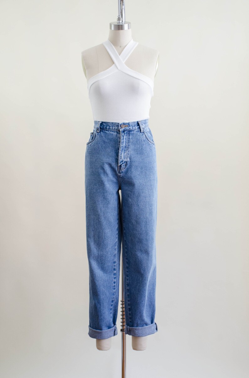 May include: A white halter top and blue denim jeans displayed on a mannequin. The top has a criss-cross design. The jeans are cuffed at the ankles.