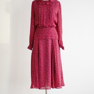 May include: A red midi dress with a white polka dot pattern. The dress has a ruffled collar and long sleeves.