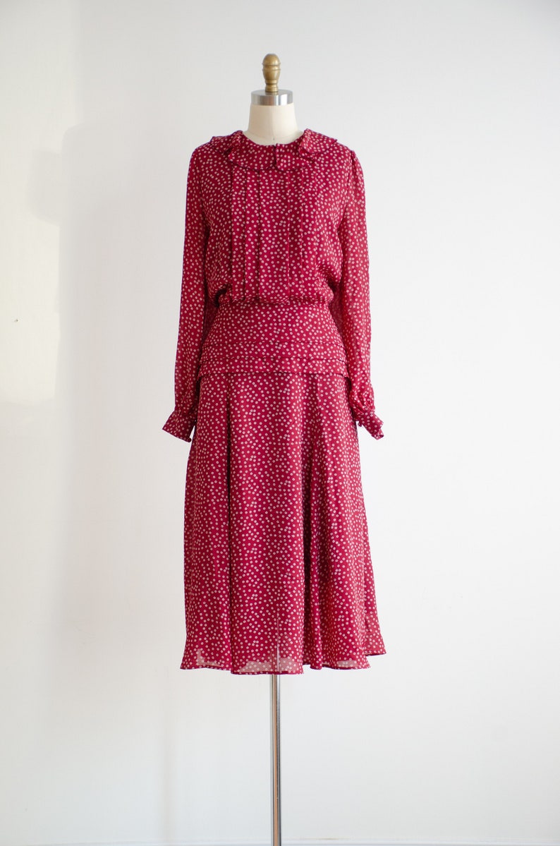 May include: A red midi dress with a white polka dot pattern. The dress has a ruffled collar and long sleeves.