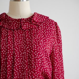 May include: A red dress with a white polka dot pattern and a ruffled collar. The dress has long sleeves and a fitted waist.