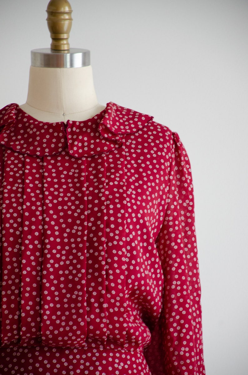 May include: A red dress with a white polka dot pattern and a ruffled collar. The dress has long sleeves and a fitted waist.
