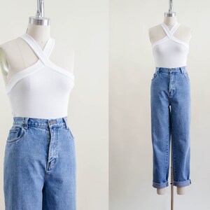 May include: A white halter top with a criss-cross design paired with light blue denim jeans. The jeans have a high waist and a straight leg fit. The jeans are cuffed at the ankles.