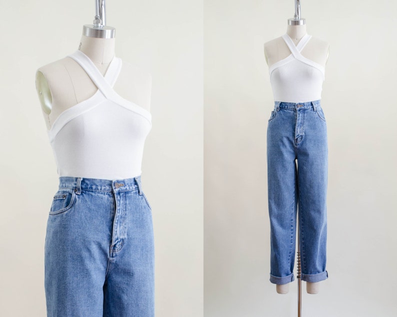 May include: A white halter top with a criss-cross design paired with light blue denim jeans. The jeans have a high waist and a straight leg fit. The jeans are cuffed at the ankles.