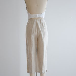 Puede incluir: Un pantal&oacute;n de lino beige de cintura alta y pierna ancha. El pantal&oacute;n est&aacute; en un maniqu&iacute; y se muestra desde atr&aacute;s.
