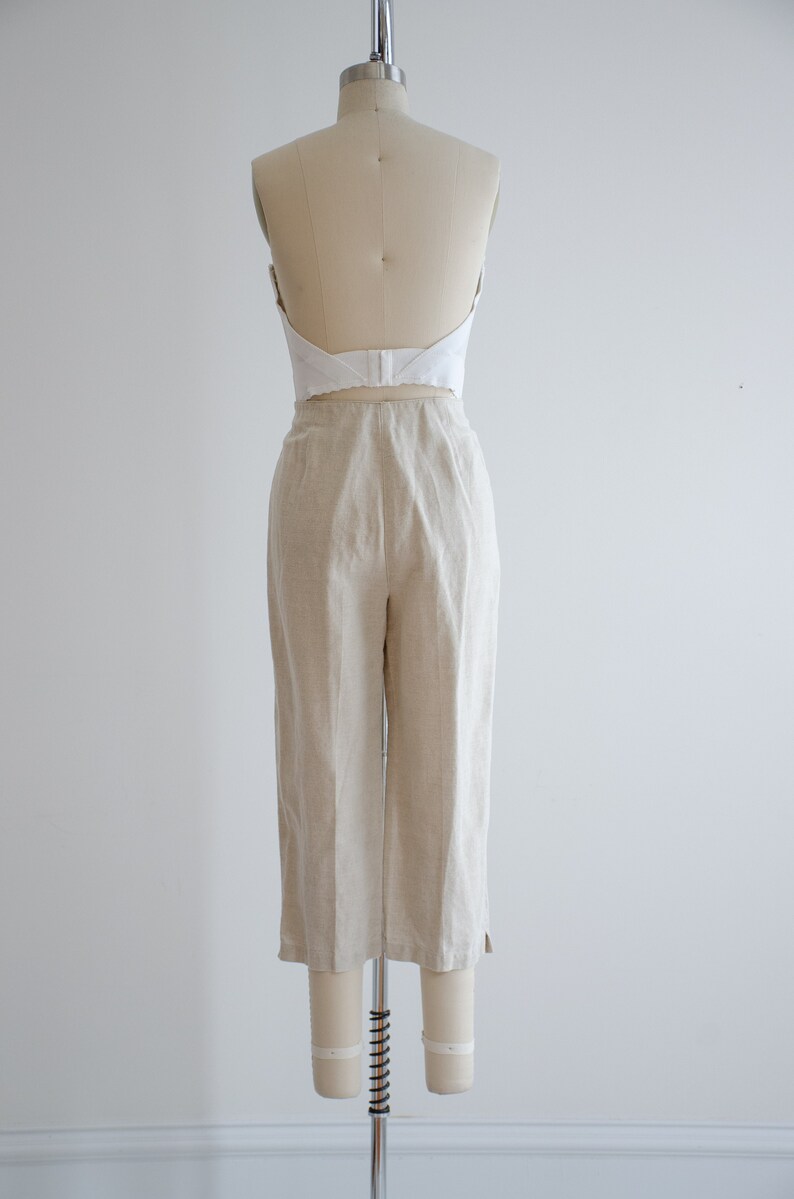 Puede incluir: Un pantal&oacute;n de lino beige de cintura alta y pierna ancha. El pantal&oacute;n est&aacute; en un maniqu&iacute; y se muestra desde atr&aacute;s.