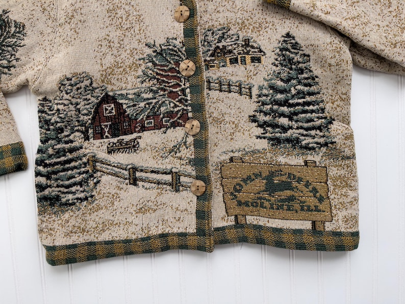 Puede incluir: Un c&aacute;rdigan beige con una escena de invierno tejida en la tela. La escena incluye una granja, &aacute;rboles y un letrero que dice "John Deere Moline, Ill."