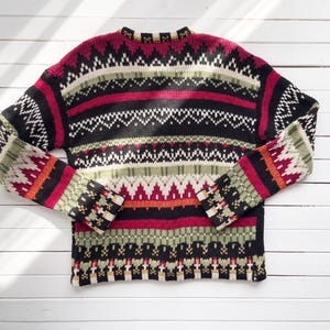 May include: A colorful, patterned sweater with a crew neck. The sweater features horizontal stripes in black, red, white, green, and orange. The sleeves and body have geometric designs. The sweater is made of a knitted material.