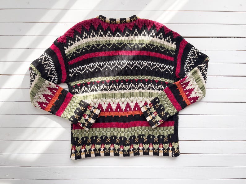 May include: A colorful, patterned sweater with a crew neck. The sweater features horizontal stripes in black, red, white, green, and orange. The sleeves and body have geometric designs. The sweater is made of a knitted material.
