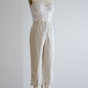 Puede incluir: Un top de encaje blanco combinado con pantalones de lino beige. Los pantalones tienen cintura alta y pierna recta.