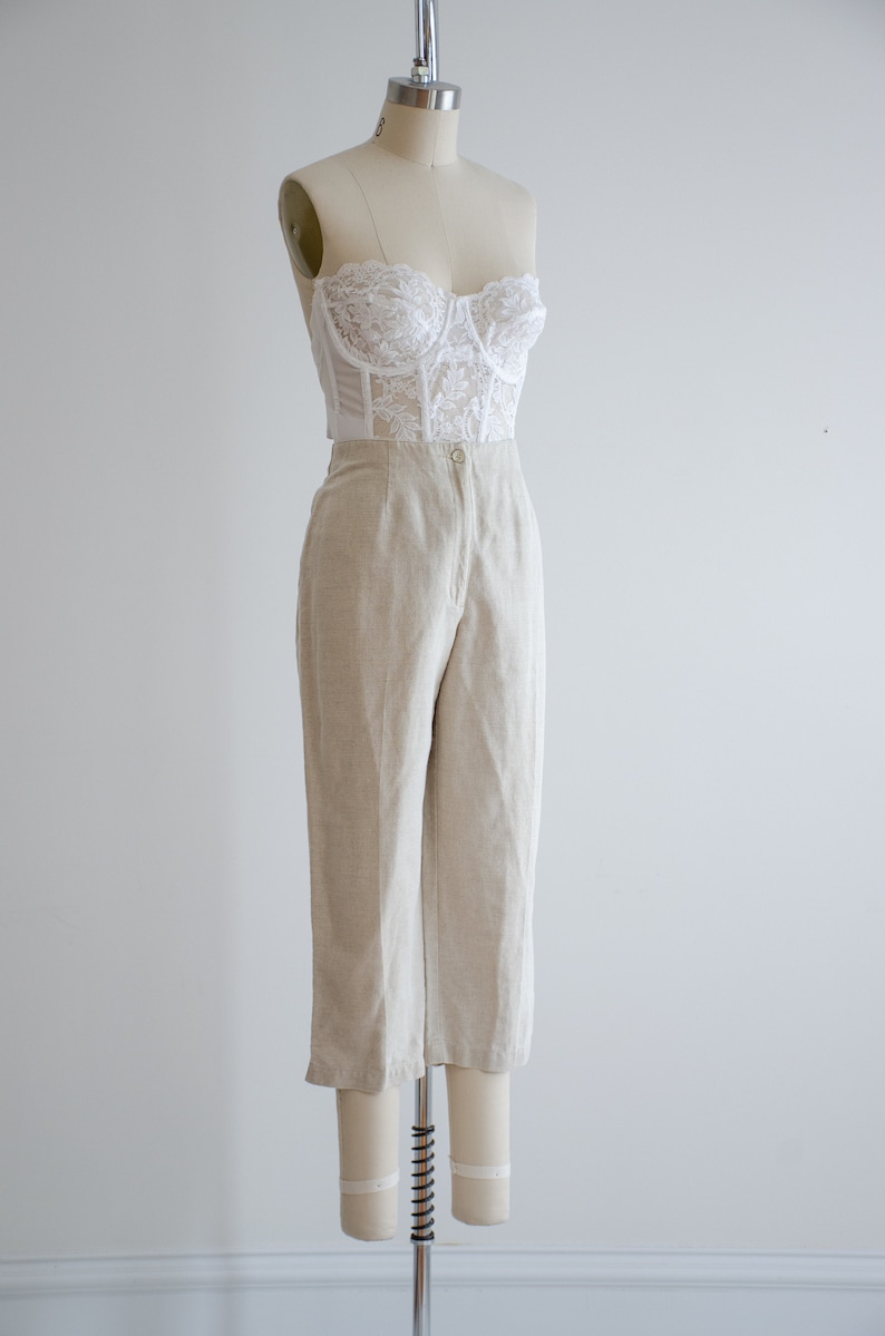 Puede incluir: Un top de encaje blanco combinado con pantalones de lino beige. Los pantalones tienen cintura alta y pierna recta.