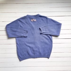 May include: A light blue knitted cardigan with a floral embroidery design on the back.