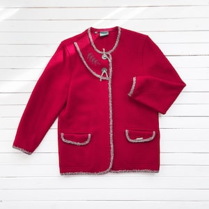 May include: A red wool cardigan with a silver trim and a leaf design on the collar. The cardigan has a button closure and two pockets.