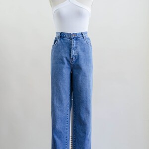 May include: A white halter top with a criss-cross design paired with blue denim jeans. The jeans have a classic straight leg fit. The outfit is displayed on a mannequin against a plain background.