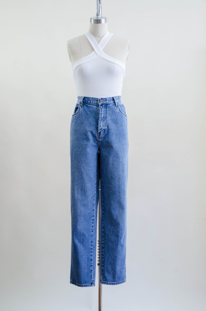 May include: A white halter top with a criss-cross design paired with blue denim jeans. The jeans have a classic straight leg fit. The outfit is displayed on a mannequin against a plain background.