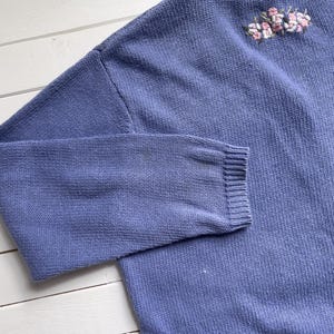 May include: A light blue knitted jumper with a floral embroidery design.