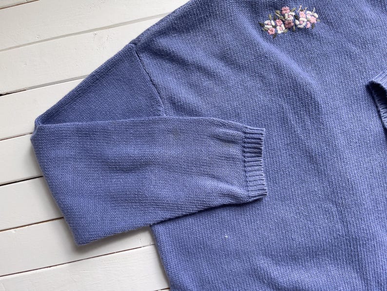 May include: A light blue knitted jumper with a floral embroidery design.