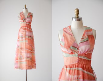 May include: A sleeveless maxi dress with a V-neckline and a button-up front. The dress is made of a sheer fabric with a peach, pink, and green abstract print.