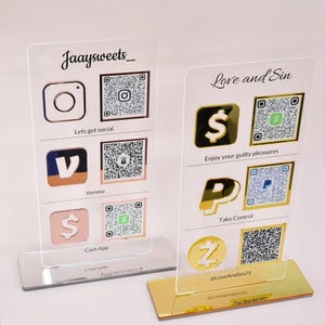Op de afbeelding: Twee heldere acryl display stands met social media iconen en QR codes. E&eacute;n stand heeft de tekst "Jaaysweets_" en "Lets get social". De andere stand heeft de tekst "Love and Sin" en "Enjoy your guilty pleasures".