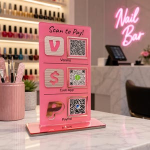 May include: A pink acrylic payment display with the text "Scan to Pay!" and QR codes for Venmo, Cash App, and PayPal. The display is on a marble surface, with a nail bar sign in the background.