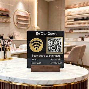 Könnte beinhalten: Ein schwarzes Schild mit goldenen Akzenten, das ein WLAN-Symbol und einen QR-Code zeigt. Der Text lautet "Be Our Guest" und "Scan code to connect!" mit Netzwerk- und Passwortdetails. Das Schild steht auf einem Holzsockel.