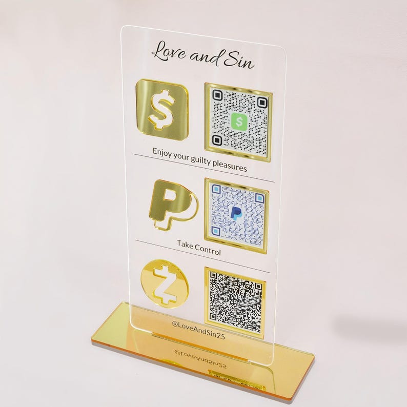 Op de afbeelding: Een helder acryl bord met gouden accenten en de tekst "Love and Sin". Het bord toont gouden iconen voor een dollarteken, PayPal en een Z, samen met bijbehorende QR-codes. De basis is goudkleurig en het bord bevat de zinnen "Enjoy your guilty pleasures" en "Take Control."