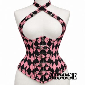 May include: A pink and black harlequin diamond patterned corset featuring a halter neck strap, a central vertical zipper, and four horizontal buckle straps with silver-toned metal hardware. The garment has a cutout chest design and silver studs.