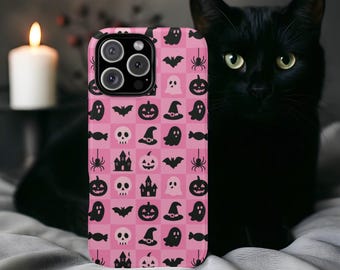 Könnte beinhalten: Eine pinkfarbene Handyhülle mit einem Halloween-Motiv mit Geistern, Fledermäusen, Kürbissen, Spinnen und Totenköpfen. Die Hülle hat ein kariertes Design und einen schwarzen Kameraobjektivbereich. Im Hintergrund ist eine schwarze Katze.