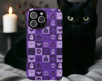 Könnte beinhalten: Eine lila Handyhülle mit einem Halloween-Muster mit Geistern, Fledermäusen, Kürbissen und Totenköpfen. Daneben sitzt eine schwarze Katze mit gelben Augen. Im Hintergrund eine brennende weiße Kerze.