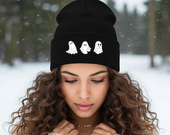 Puede incluir: Gorro negro con tres diseños de fantasmas blancos. El gorro está hecho de un material suave y tejido. Los fantasmas tienen diferentes expresiones faciales. El fondo es una escena nevada al aire libre.