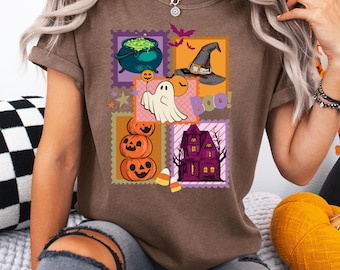 May include: A brown t-shirt with a Halloween design. The design features a cauldron with green liquid, a witch's hat, a ghost, pumpkins, a haunted house, and the word "Boo!" arranged like stamps.