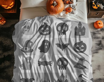 May include: A gray and white Halloween-themed blanket featuring a repeating pattern of pumpkins, ghosts, bats, skulls, witch hats, and haunted houses. The bed is decorated with pumpkins and a decorative pillow.