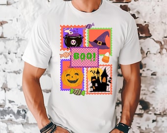May include: White t-shirt with a Halloween design. The design includes a cauldron, witch's hat, pumpkin, haunted house, candy corn, and the word "BOO!" in a playful font, all within postage stamp-like frames. The design is colourful and fun.