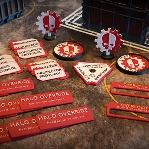 Pode incluir: Uma coleção de fichas e marcadores de jogo vermelhos e brancos. As fichas apresentam um design de caveira e engrenagem, com texto como "HALO OVERRIDE" e "OVERLOAD". Existem também vários marcadores em forma de engrenagem.