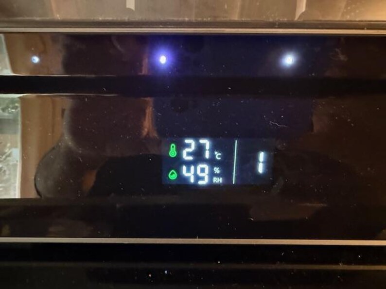 Puede incluir: Una pantalla digital que muestra la temperatura a 27 grados Celsius y la humedad al 49%. La pantalla tambi&eacute;n muestra el n&uacute;mero 1. La pantalla es verde sobre un fondo negro.