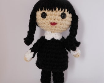 May include: A handmade crochet doll with black hair, a black dress, and a white collar. The doll has a light skin tone, black button eyes, and a red mouth. The doll's arms and legs are also crocheted.