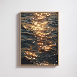 Könnte beinhalten: Ein rechteckiger gerahmter Wandkunstdruck mit einer Fotografie von dunkelblauem Meerwasser und einem vertikalen Pfad aus goldenem Sonnenlicht, das sich auf der welligen Oberfläche spiegelt. Der Rahmen besteht aus hellem Holz mit einem dünnen Profil.