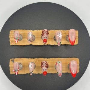 May include: A set of ten artificial nails, each with a different Christmas-themed design. The designs include candy canes, snowflakes, reindeer faces, and holly berries. The nails are displayed on a wooden holder.