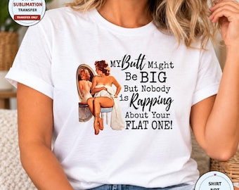 May include: A white short-sleeved t-shirt featuring a graphic of a pin-up style illustration of a person sitting on a stool in front of a mirror, with the text: MY Butt Might Be BIG But Nobody is Rapping About Your FLAT ONE!