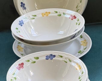 May include: A set of white ceramic bowls and plates featuring a delicate hand-painted pattern of small blue, yellow, and red flowers with green leaves. The dinnerware has a subtle wavy rim design and a smooth, glossy finish on all pieces.
