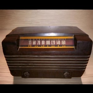 May include: A vintage brown radio with a horizontal design. The radio dial displays numbers from 55 to 160, with the word "Radio" below. Two knobs are visible on the bottom left and right. The radio has a retro aesthetic.