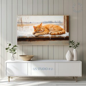 May include: A framed painting depicts a sleeping orange tabby cat resting on a snowy ledge. The background shows a winter landscape with bare trees and a cloudy sky. The artwork is displayed above a white cabinet with the text "- US STUDIO 4 U -" at the bottom.