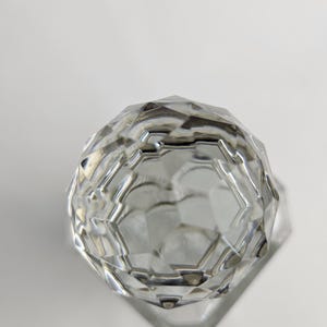 K&ouml;nnte beinhalten: Ein klares, facettiertes Glasobjekt mit geometrischem Design. Das Objekt hat eine abgerundete Oberseite und eine flache, sechseckige Basis. Die Facetten fangen das Licht ein und erzeugen einen funkelnden Effekt. Es ist wahrscheinlich ein dekorativer Gegenstand oder ein Beh&auml;lter.