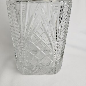 K&ouml;nnte beinhalten: Eine klare, rechteckige Glasdekanter mit einem silberfarbenen Verschluss. Der Dekanter hat ein Diamanten- und vertikales Linienmuster. Das Glas ist dick und hat ein facettiertes Design, das einen funkelnden Effekt erzeugt. Der Dekanter ist leer.