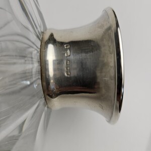 K&ouml;nnte beinhalten: Nahaufnahme einer klaren Glasdekanter mit einem silberfarbenen Metallsockel. Das Glas hat ein geripptes Design. Der Metallsockel hat Markierungen. Der Dekanter wird wahrscheinlich zum Servieren von Getr&auml;nken verwendet.