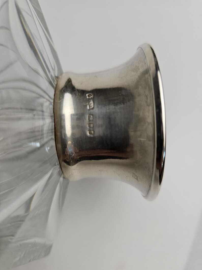 K&ouml;nnte beinhalten: Nahaufnahme einer klaren Glasdekanter mit einem silberfarbenen Metallsockel. Das Glas hat ein geripptes Design. Der Metallsockel hat Markierungen. Der Dekanter wird wahrscheinlich zum Servieren von Getr&auml;nken verwendet.